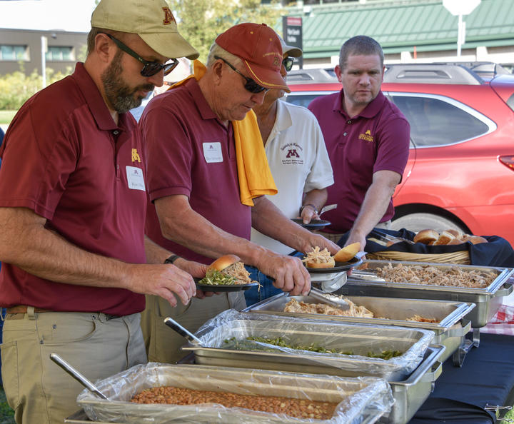 several men load their plates with barbecue under tent 